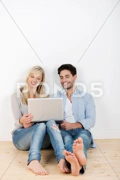 Couple using laptop while sitting on hardwood floor Stock Photos