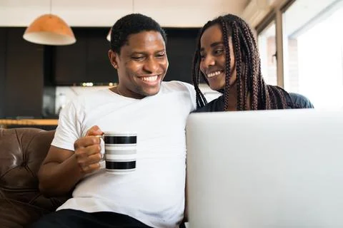 Couple using laptop while sitting on couch at home. Stock Photos