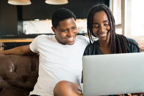 Couple using laptop while sitting on couch at home. Stock Photos