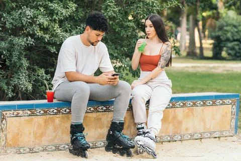 Couple using mobile while drinking soft drink in a park with inline skates on Stock Photos