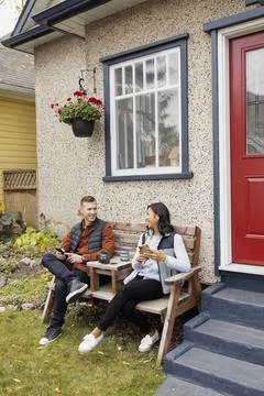 Couple using phone, talking on bench at front porch Fotos Stock