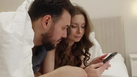 Couple using smartphone in bed, cozy morning routine Stock Footage 327927894