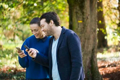 Couple using smartphones while walking in woods Stock Photos