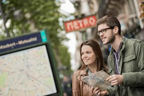 A couple using a street map beside an information sign under a metro sign Foto stock