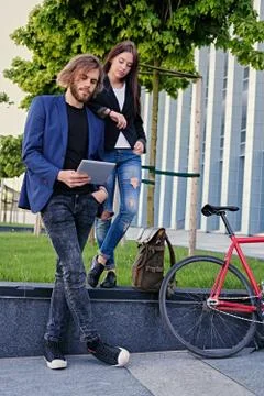 A couple using a tablet PC with fixed red bicycle in a park on background. Stock Photos