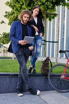A couple using a tablet PC with fixed red bicycle in a park on background. Stock Photos