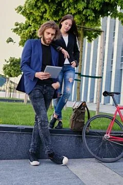 A couple using a tablet PC with fixed red bicycle in a park on background. Stock Photos