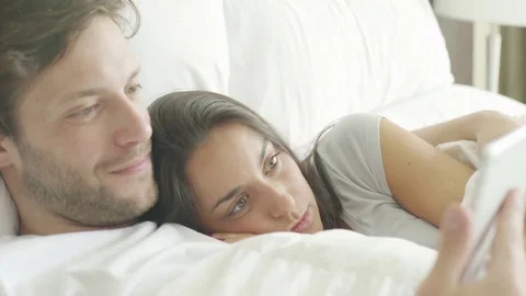 Couple using wireless device in bed Stock Footage 75176968