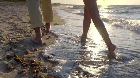 Couple Walk Along Beach, Closeup Of Legs/Bare Feet, Waves Crash At Their Feet Stock Footage