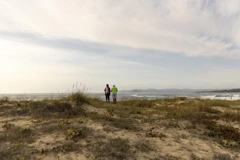 A couple is walking on a beach with a cloudy sky in the background Fotos Stock