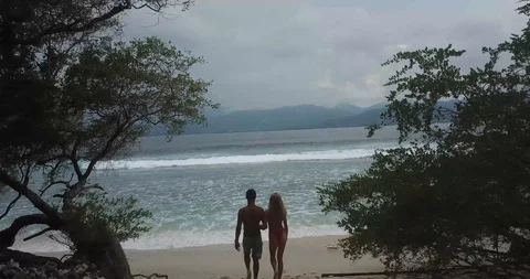 Couple Walking to Beach Through Trees Drone Shot Stock Footage 106236673