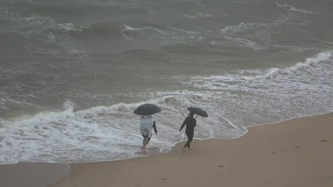 Couple walking on beach with umbrellas while its raining outside Video stock 121973875