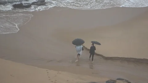 Couple walking on beach with umbrellas while its raining outside Video stock 121973891