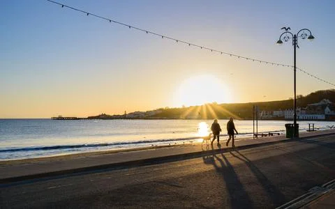 Couple walking the dog at sunrise along the beach at Swanage Bay Stock Photos