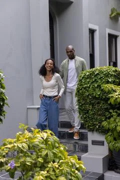 Couple walking down tiled stone steps at gray townhouse entrance, woman smiling Fotos Stock