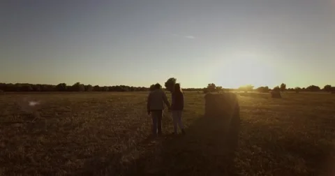Couple is walking on a field at sunset with trees and haystacks Stock Footage 68093298