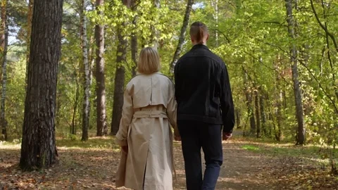 Couple walking hand in hand through a serene forest path, surrounded by vibrant Stock Footage 316872903