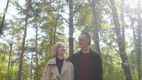 Couple walking hand in hand through a serene forest path, sharing smiles and Stock Footage 316873014