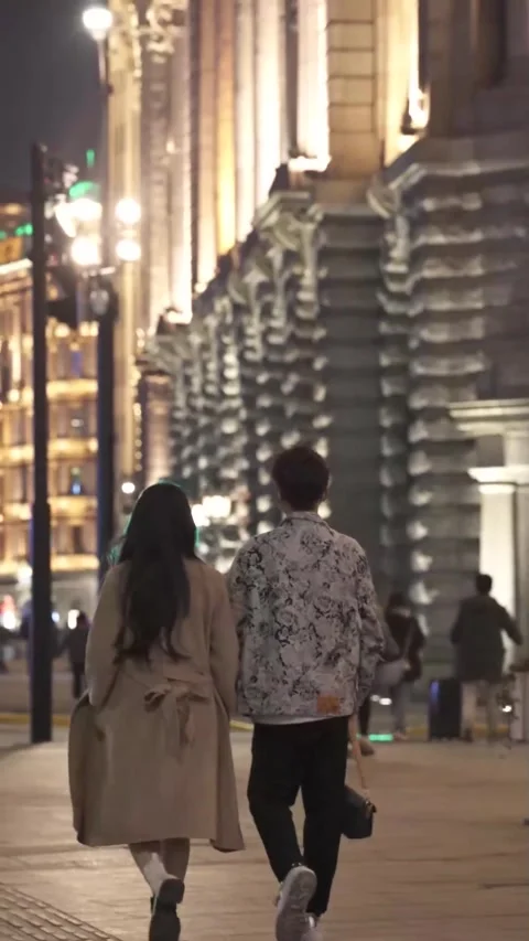 Couple Walking at Night Along Illuminated City Street with Historic Architecture Stock Footage 326604953