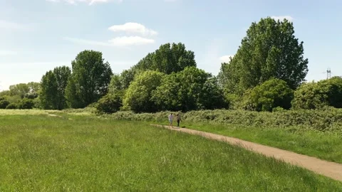 Couple walking on path leading on edge of meadow around trees and shrubs Stock-Footage 155823444