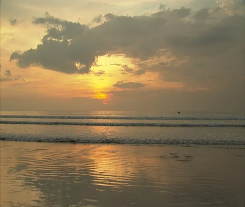 Couple walking on shore with ocean waves breaking on beach in orange sunlight Stock Footage 86747514