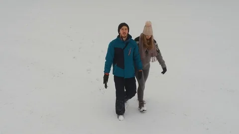 Couple walking in the snow as the camera flies around them and then follows them Stock Footage 94483169