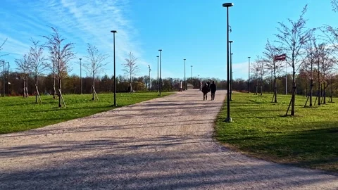 Couple walking on a sunny park pathway with a Latvian flag waving Stock Footage 337791241
