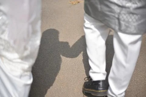 Couple walking together casting a shadow holding hands on pavement Stock Photos