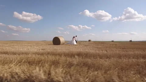 Couple walking together through summer harvested field with straw bales. Aerial Stock Footage 242426271
