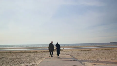 A couple walking towards ocean on the cold sunny beach Stock Footage 143252955