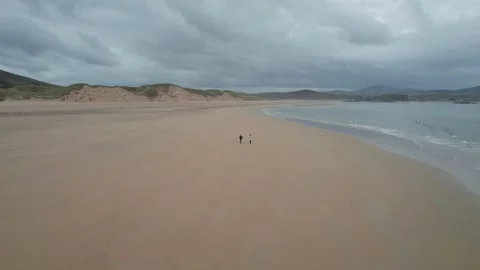 Couple walks along sandy beach under cloudy sky in Donegal Stockbeeldmateriaal 310240297