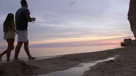 A couple walks along the seashore with glasses of wine they smile and kiss Stock Footage