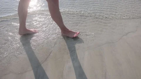 Couple walks on the beach at sunset. The camera only takes the legs of the Stock Footage 233054833