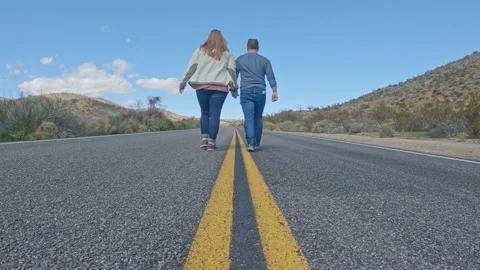 Couple Walks Down Road Together Holding Hands In Joshua Tree National Park Stock Footage 155032840