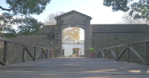 Couple walks into frame looking at the gate of Colonia de Sacramento Vídeos de archivo 92349515