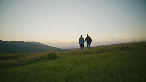 Couple walks hand in hand across grassy field as the sun sets behind the Stock Footage 345683677