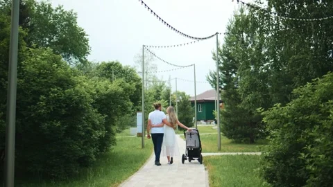 Couple walks with stroller through park path amid lush trees Stock Footage 340885991