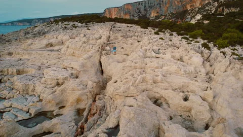 Couple walks on wind-swept white limestone plateau near sheer cliffs on Alaties Stock Footage 341352012