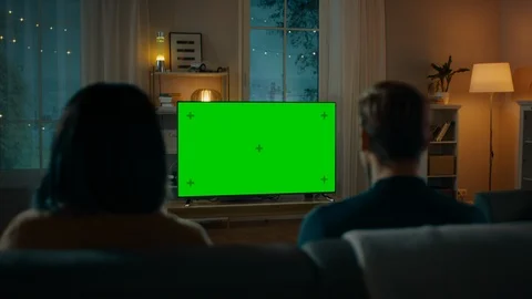 Couple Watches Green Mock-up Screen TV while Sitting on a Couch in Living Room Stock Footage