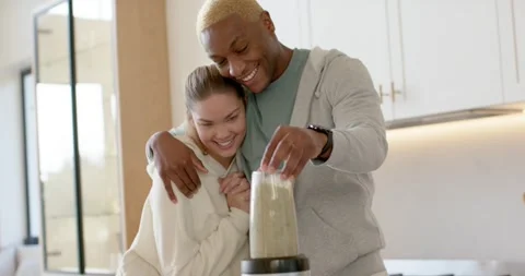 Couple watching man pressing down blender cup on base at kitchen island, making Stock Footage 345607464
