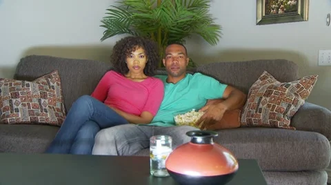 Couple watching movie on couch while eating popcorn Stock-Footage 7730407