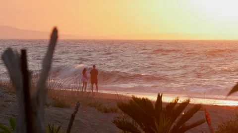 A couple watching the sunset with big waves and orange light Stock Footage 157287860
