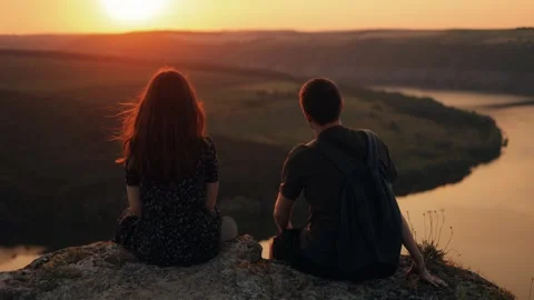 . Couple watching sunset, talking on cliff edge above river. back view. Stock Footage 246386015
