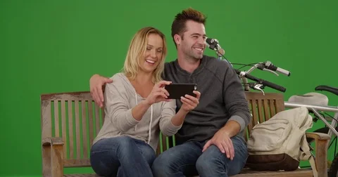 Couple watching videos on smartphone together on a bench on green screen Stock Footage