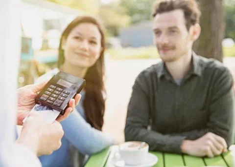 Couple watching waitress using credit card reader at outdoor cafe Stock Photos