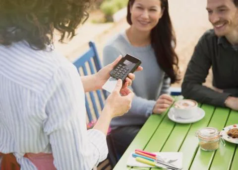 Couple watching waitress using credit card reader at outdoor cafe Stock Photos