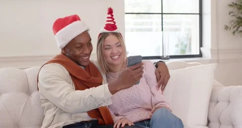 Couple wearing Santa hat, tree headband laughing on sofa while man tilting Stock Footage 343469387