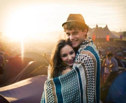 Couple wrapped in a blanket outside tents at music festival Stock Photos