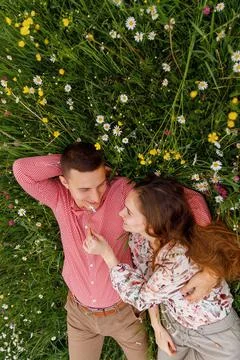 Couple of young people lying down on grass in field of flowers . Stock Photos