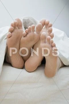 A Couple's Feet Lying In Bed